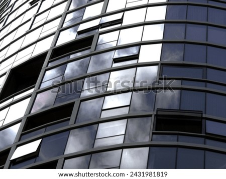 This high-resolution stock photo captures the essence of urban sophistication with its detailed view of a modern building's curved glass facade, reflecting the dynamic skies above.