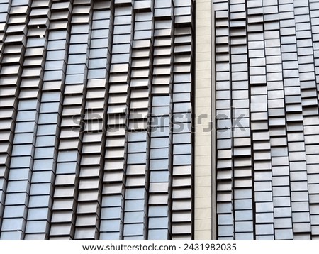 This high-resolution stock photo captures the rhythmic beauty of repeating patterns on the exterior of an urban building. The striking contrast between the light and dark tiles is captivating.