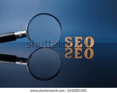 Wooden word SEO and magnifying glass on a black acrylic board with reflection
