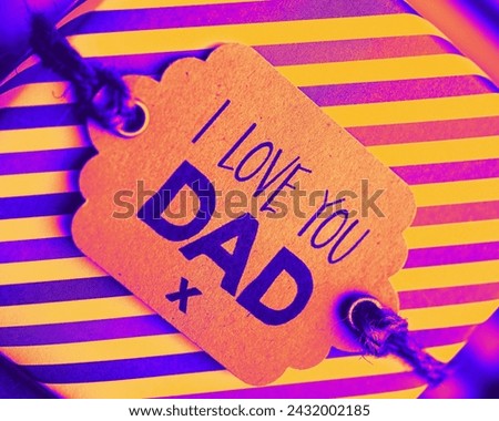The image is of a person holding a sign with the words "I LOVE YOU DAD" written on it. The sign features magenta and violet colors and is a form of art with handwritten font.