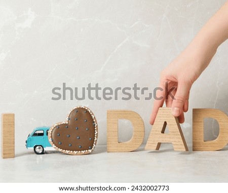 The image shows a hand reaching for a wooden block labeled "DAD" with additional items like a wheel, vehicle, sandal, measuring stick, and miniature. Royalty-Free Stock Photo #2432002773