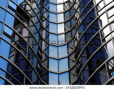 This high-resolution stock photo captures the geometric elegance of a modern building's reflective glass facade, creating a visual puzzle of the sky and surrounding structures mirrored upon it.