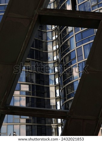 This high-resolution stock photo captures a striking contrast in urban architecture, with the rigid lines of a metallic structure framing the curved glass facade of a modern building.