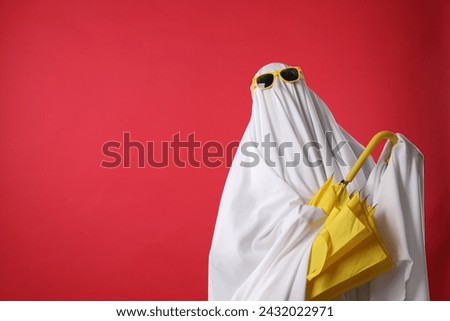 Person in ghost costume and sunglasses holding yellow umbrella on red background, space for text