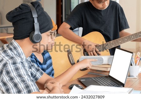 Asian boys wear beanie and headphones and learning music lesson on laptop in media library of their school, teens' lifestyle concept, new edited.