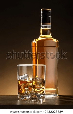 Whiskey with ice cubes in glass and bottle on wooden table