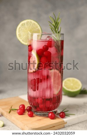 Tasty cranberry cocktail with rosemary and lime in glass on gray background