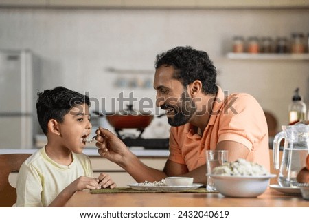 Happy father feeding His child by talking and encouraging at home - concept of fatherhood, affection and family bonding Royalty-Free Stock Photo #2432040619