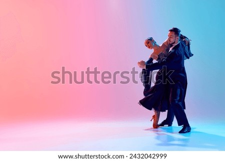 Beautiful young man and handsome woman, ballroom dancers making performance, dancing against gradient pink blue background in neon light. Concept of dance class, hobby, art, dance school, talent