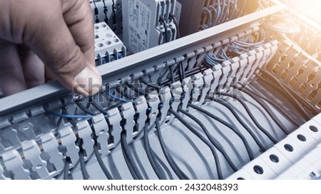 an electrician's hand is opening or closing the circuit cable cover on the electrical control panel board.Check and repair electrical trouble concept. Royalty-Free Stock Photo #2432048393