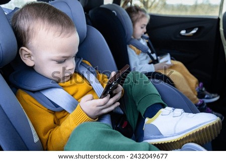 Side view of brother and sister on car back seat holding smart phones while traveling.