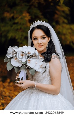 Portrait. A brunette bride in a dress and a veil, with a chic crown, poses with a bouquet. Silver jewelry. Beautiful makeup and hair. Autumn wedding. celebration