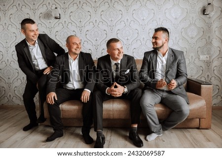 A young groom and his funny friends pose for the camera. A group of young people hug the groom and cheerfully congratulate him. Happy friends. Friends in the room. Wedding day.