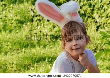 Portrait of a smiling child girl wearing a headband with bunny ears in the garden. Easter religious holiday concept. Copy space