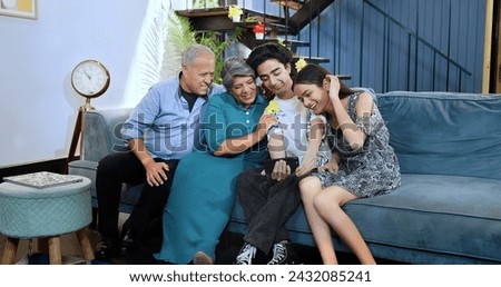 Happy Indian excited family sitting on sofa smiling teenage girl hold smartphone taking selfie at house. Old aged grandparents couple make funny pose photo or record video vlog enjoy weekend together