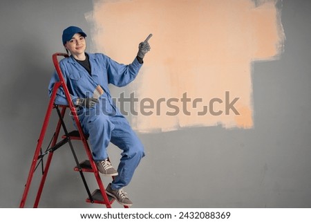 Painter woman sitting on ladder and pointing to the side on wall to present a product at home. Copy space