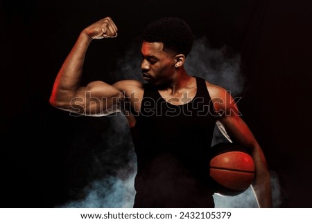 Basketball player side lit with red color holding a ball against hazy smoke fog background. Serious african american man showing muscles