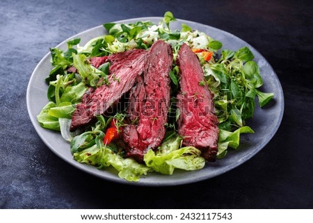 Traditional barbecue bavette beef steak slices with lambs salad and iceberg lettuce served as close-up on a design plate  Royalty-Free Stock Photo #2432117543
