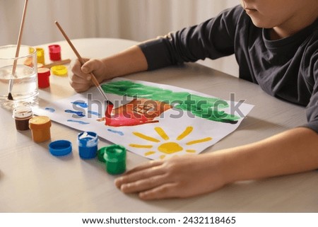 Little boy drawing picture with brush at wooden table indoors, closeup. Child`s art