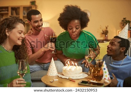 Portrait of adult Black woman blowing candles on Birthday cake and enjoying party celebration with friends at home