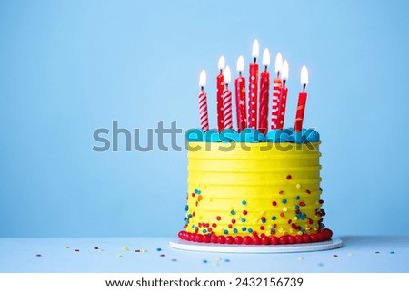 Colorful celebration birthday cake with yellow frosting and red birthday candles against a blue background