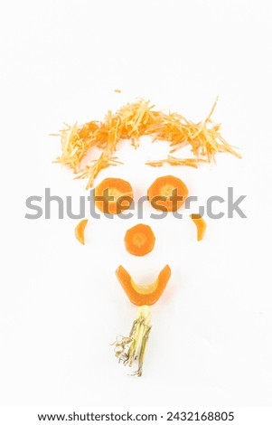 A smiling face made from slices of a carrot, grated carrot messy hair and a beard of green leaves. Isolated on a white background studio shot high quality image close-up macrophotograph. Overhead view