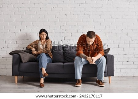 young frustrated interracial couple sitting on couch in living room, family divorce concept Royalty-Free Stock Photo #2432170117