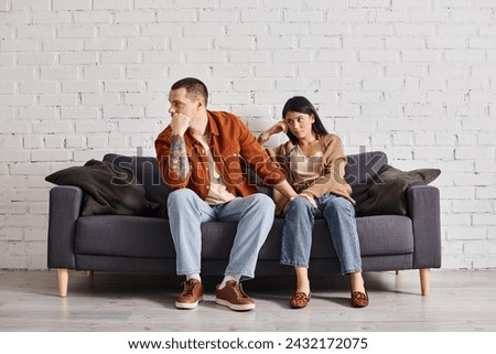 young interracial couple in quarrel sitting on couch in living room at home, divorce concept Royalty-Free Stock Photo #2432172075