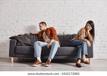 young interracial couple with emotional distress sitting on couch in living room, divorce concept Royalty-Free Stock Photo #2432172083