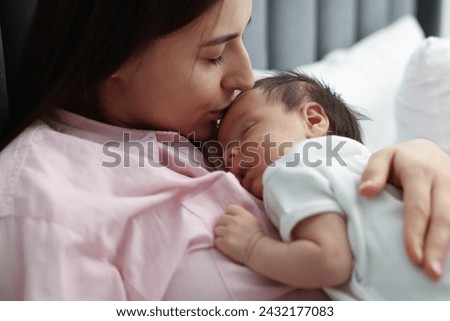 Mother kissing her sleeping newborn baby in bed