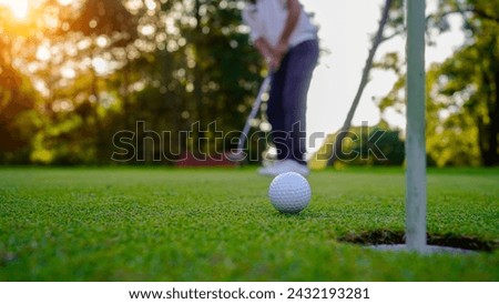 Golfer putting ball on the green golf, lens flare on sun set evening time. Golfer action to win after long putting golf ball in to the hole.                                  Royalty-Free Stock Photo #2432193281