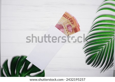 One Hundred Thousand Rupiah Bills Coming out from White Envelop on a White Wooden Background