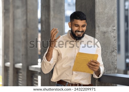 A cheerful man stands outside, smiling widely as he reads a letter from envelope. The image captures a sense of joy, surprise, and positive emotion, ideal for concepts of good news, communicat Royalty-Free Stock Photo #2432209971