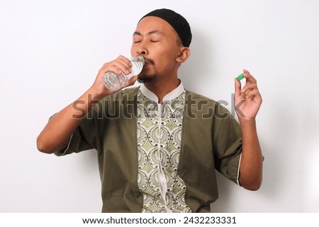 An Indonesian Muslim man in koko and peci breaks his Ramadan fast with a bottle of mineral water at sunset