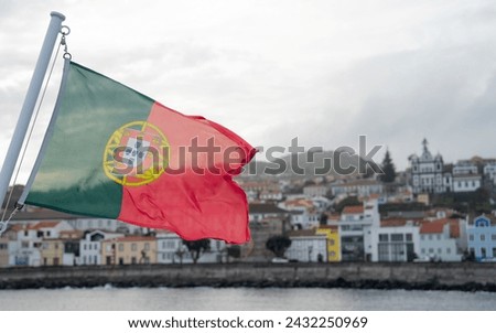 The Portuguese flag on a ferry with the significant port of Horta in the background. It is the oldest port in Europe. Horta, Azores , Portugal 