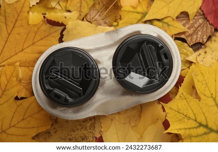 Cardboard cups for hot drinks in a tray on fallen autumn leaves