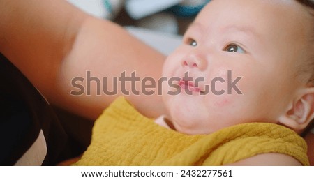 Joyful baby in a mustard bib smiling while cradled in a parent's arms, with a soft-focus background enhancing the child's cheerful expression