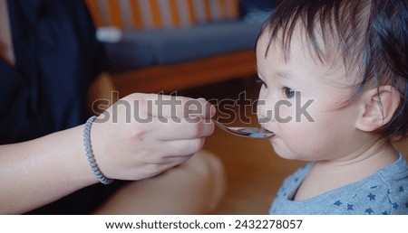 An eager toddler opens wide for a spoonful of food during a messy yet joyful feeding time at home Royalty-Free Stock Photo #2432278057