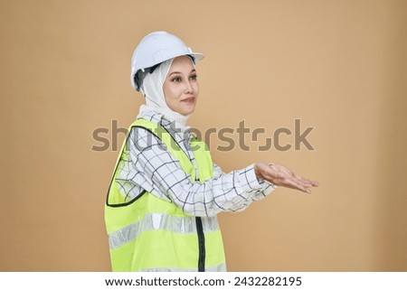 Asian hijab girl engineer in yellow  vest and wearing a safety helmet, hold out her hand in a begging gesture isolated on background in studio.