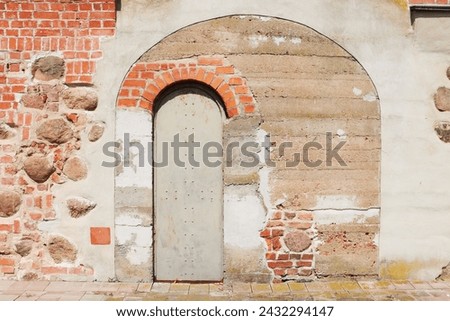 An ancient, time-damaged wall made of stone, red brick, iron doors. Part of the façade of the castle wall.