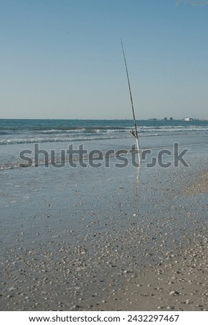Surf fishing pole stuck in the sand leaning to the left with a view out to Tampa Bay off of St Pete  Beach, Florida  in the late afternoon sun. Beach sand in the foreground and waves in the background