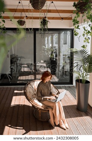 Busy young professional red-haired business woman entrepreneur holding laptop using computer working sitting in cozy chair in sunny creative green office environment. Top view, vertical photo.