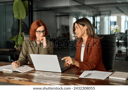Two busy female coworkers working together using computer planning marketing project. Professional business women employees looking at laptop discussing corporate software sitting at desk in office. Royalty-Free Stock Photo #2432308055