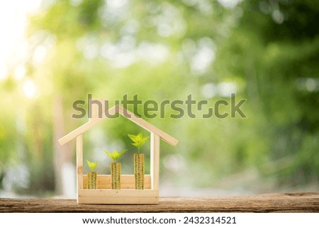 Stacked gold coins and plant growing on the top put in the wooden home model on the wood on bokeh background in the public park, Business investment and loans for real estate concept.