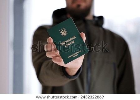Young ukrainian conscript soldier shows his military token or army ID ticket indoors close up