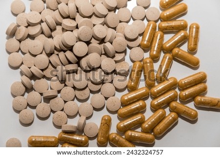 Transparent capsules with yellow powder and light brown pills on white background close up top view