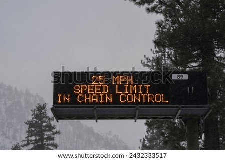Digital highway sign in Sierra Nevada mountains that reads,"25 MPH SPEED LIMIT IN CHAIN CONTROL." Captured during the onset of a winter storm.  