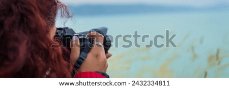Woman holding a camera by the lake in the evening
