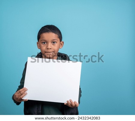 Elementery school hispanic boy looking at the camera holding a sign with room for copy