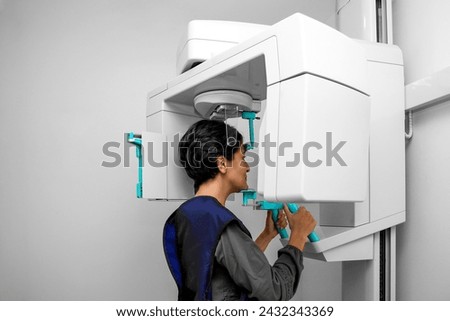 woman doing a 3D scan of the nose and oral cavity in plastic surgery clinic. blue protective vest in the X-ray room. X-ray equipment in a dental clinic. Panoramic X-ray of 3d tomography teeth. Royalty-Free Stock Photo #2432343369